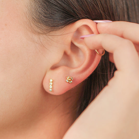 Oreja de mujer con topito en forma de flor de 4 pétalos en oro amarillo de 18 quilates con 4 cristales de color blanco, hechos en Joyería Caracas. 