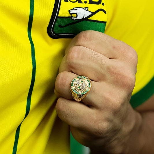 Mano la cual empuña la camisa del atletico bucaramanga y tiene en su dedo un anillo en oro amarillo de 18 quilates, este está conformado por un leopardo en el centro con cristales de color verde y blanco y en los laterales textura de piel de leopardo.