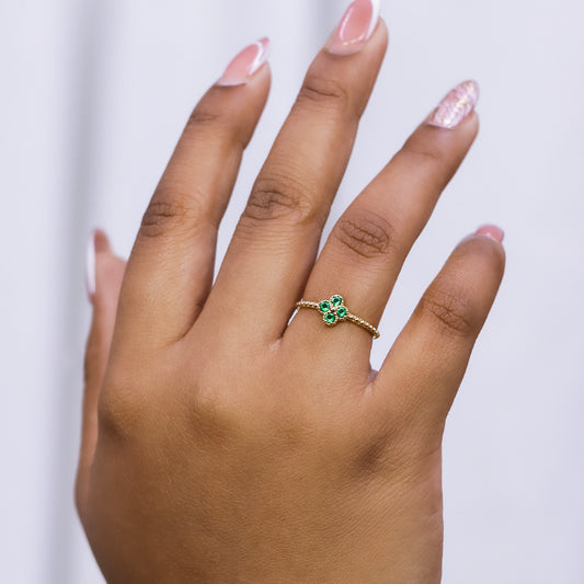 Mano de mujer con anillo en forma de trébol en oro amarillo de 18 quilates con cristales de color verde, hecho en Joyería Caracas. 