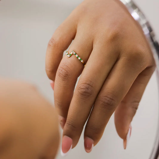 Mano de mujer con anillo en oro amarillo de 18 quilates y cristales de color blanco y verde, hecho en Joyería Caracas. 