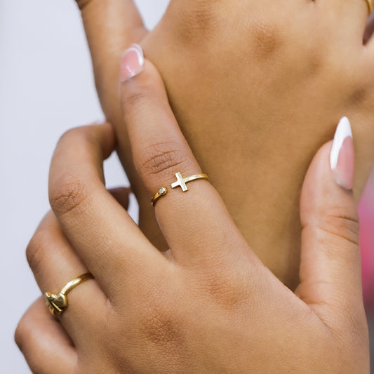 Mano de mujer con anillo en forma de cruz abierta en oro amarillo de 18 quilates y cristal de color blanco, hecho en Joyería Caracas. 