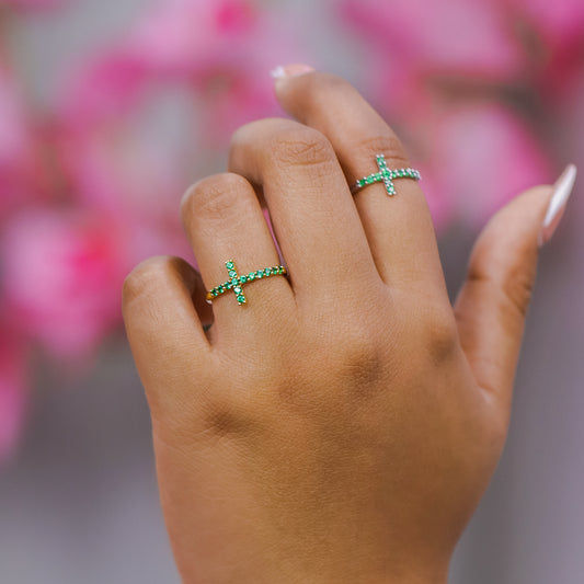 Mano de mujer con anillo en forma de cruz en oro amarillo de 18 quilates con cristales de color verde, hecho en Joyería Caracas. 