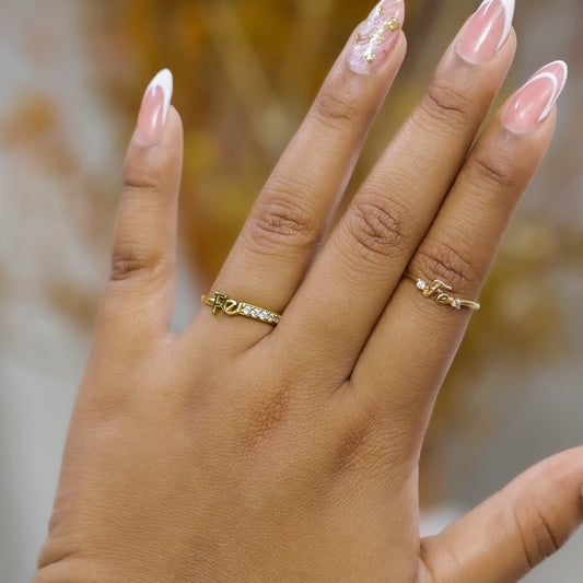 Mano de mujer usando anillo con la palabra fé en oro amarillo de 18 quilates con cristales de color blanco, hecho en Joyería Caracas. 