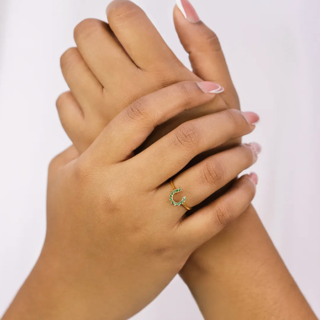 Mano de mujer usando anillo con forma de herradura en oro amarillo de 18 quilates con cristales de color verde, hecho en Joyería Caracas. 