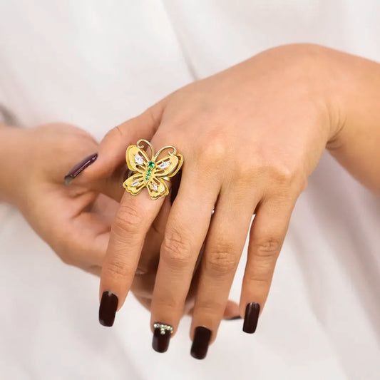 Mano de mujer con anillo en forma de mariposa en oro amarillo de 18 quilates con cristales de color verde y blanco, hecho en Joyería Caracas. 