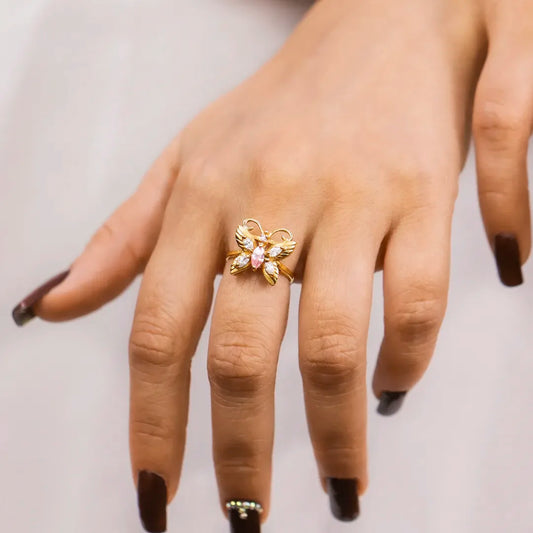 Mano de mujer con anillo en forma de mariposa en oro amarillo de 18 quilates con cristales en corte marquise color blanco y rosa, hecho en Joyería Caracas. 