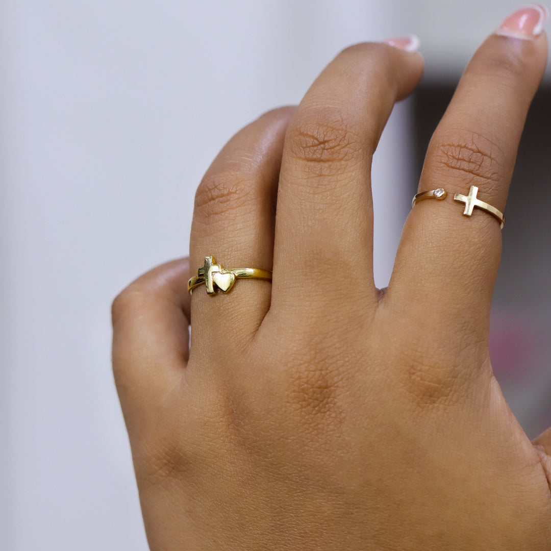 Mano de mujer usando anillo con una cruz y corazón en oro amarillo de 18 quilates, hecho en Joyería Caracas. 