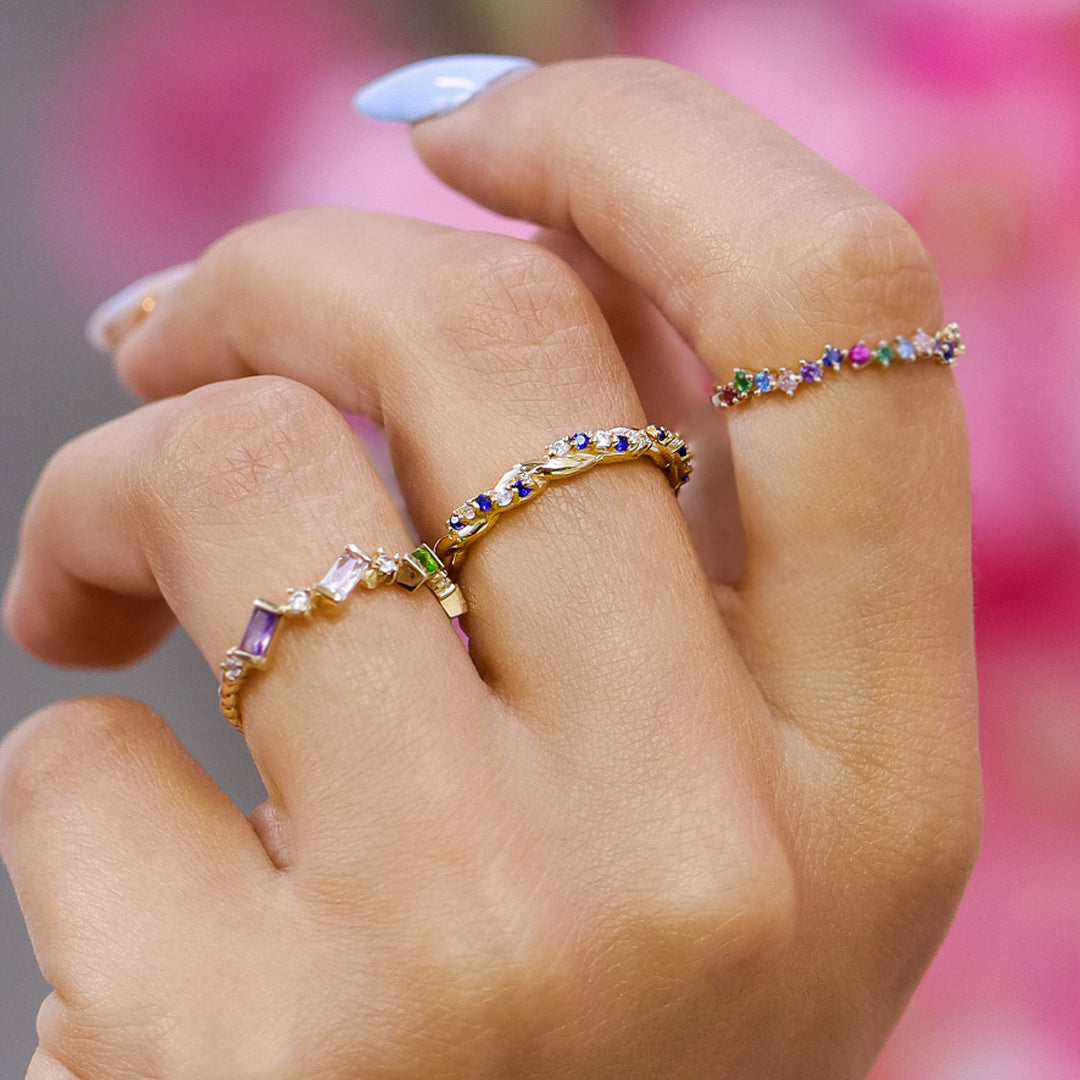 Mano de mujer con anillo entrelazado en oro amarillo de 18 quilates con cristales de color azul y blanco, hecho en Joyería Caracas. 