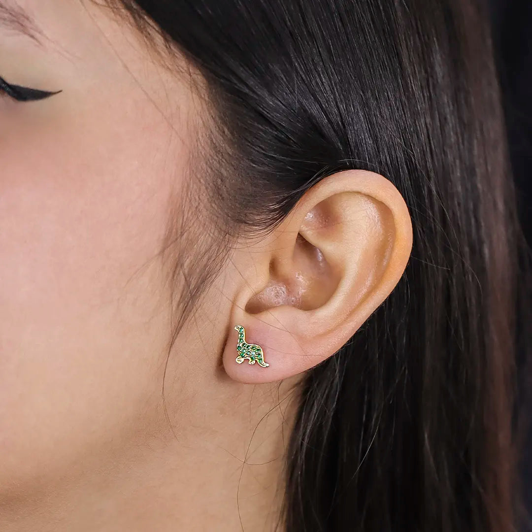 Oreja de mujer con topito en forma de dinosaurio en oro amarillo de 18 quilates con cristales de color verde, hechos en Joyería Caracas. 