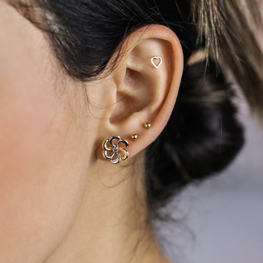 Oreja de mujer con topito en forma de flor en oro amarillo, blanco y rosa de 18 quilates, hechos en Joyería Caracas. 