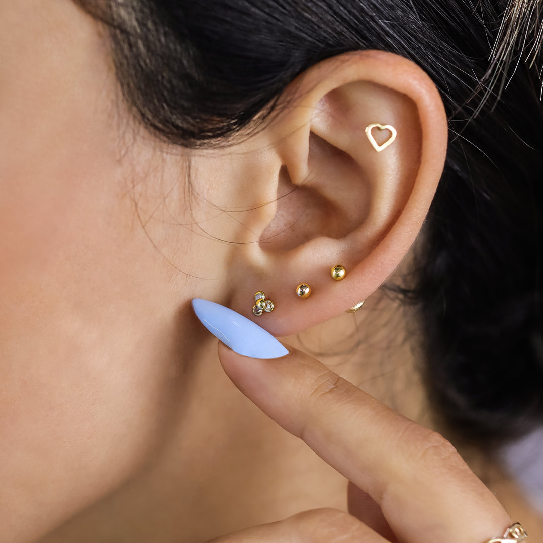 Oreja de mujer con topitos en forma de flor de loto en oro amarillo de 18 quilates con cristales de color blanco, hechos en Joyería Caracas. 