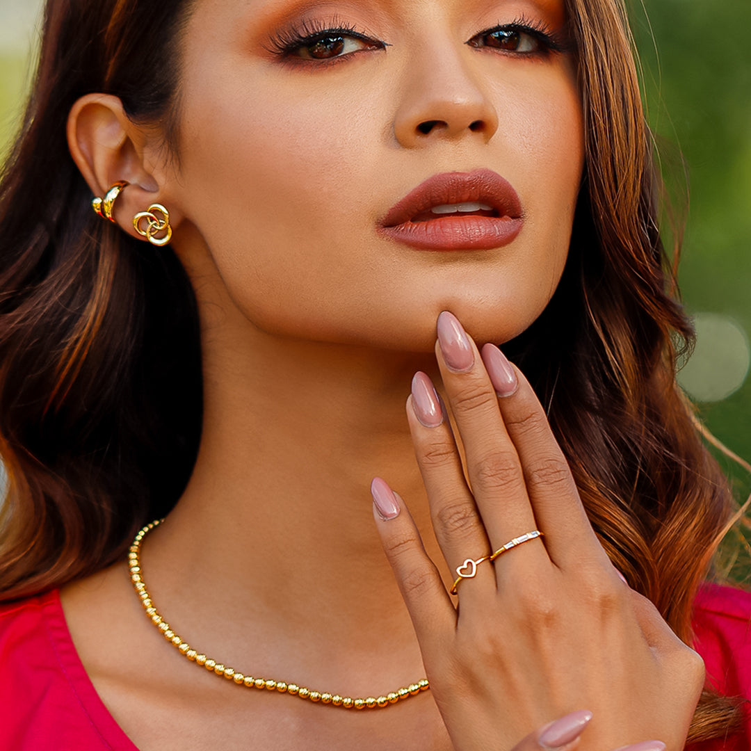 Mano la cual contiene anillo para mujer, ubicado en el dedo anular, hecho en oro 18k, color amarillo, con estilo minimalista, en forma de corazón en el centro. 