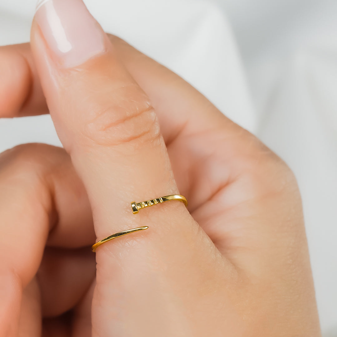 Mano donde se muestra un anillo para mujer, hecho en oro 18k, color amarillo, ubicado en el dedo pulgar de la mano, con estilo minimalista, con forma de puntilla. 