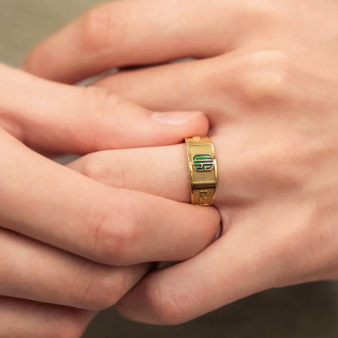 Mano con anillo de grado hecho en oro de 18k, color amarillo, el cual tiene texturas y relieves, ubicado en el dedo anular.