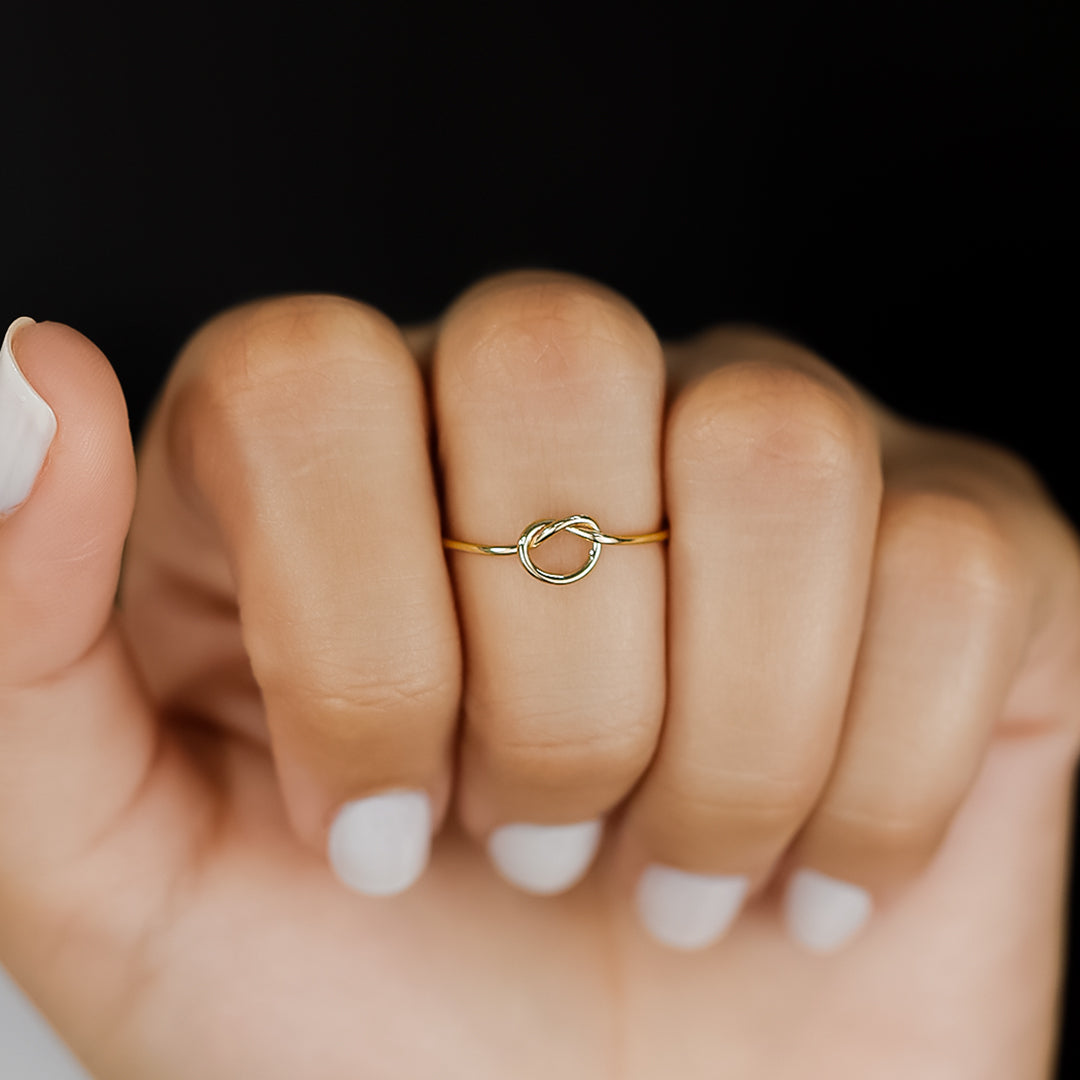 Mano con anillo para mujer, hecho en oro de 18k, color amarillo, tiene un estilo minimalista, en forma de nudo en el centro. 