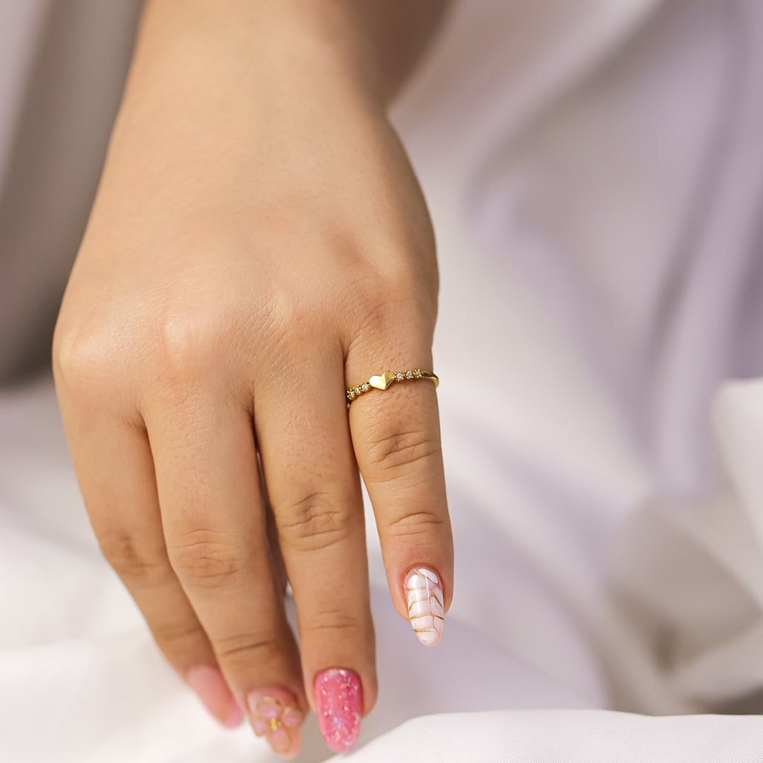 Mano de modelo posando con un anillo de corazón con 3 piedras a los lados en oro 18k.