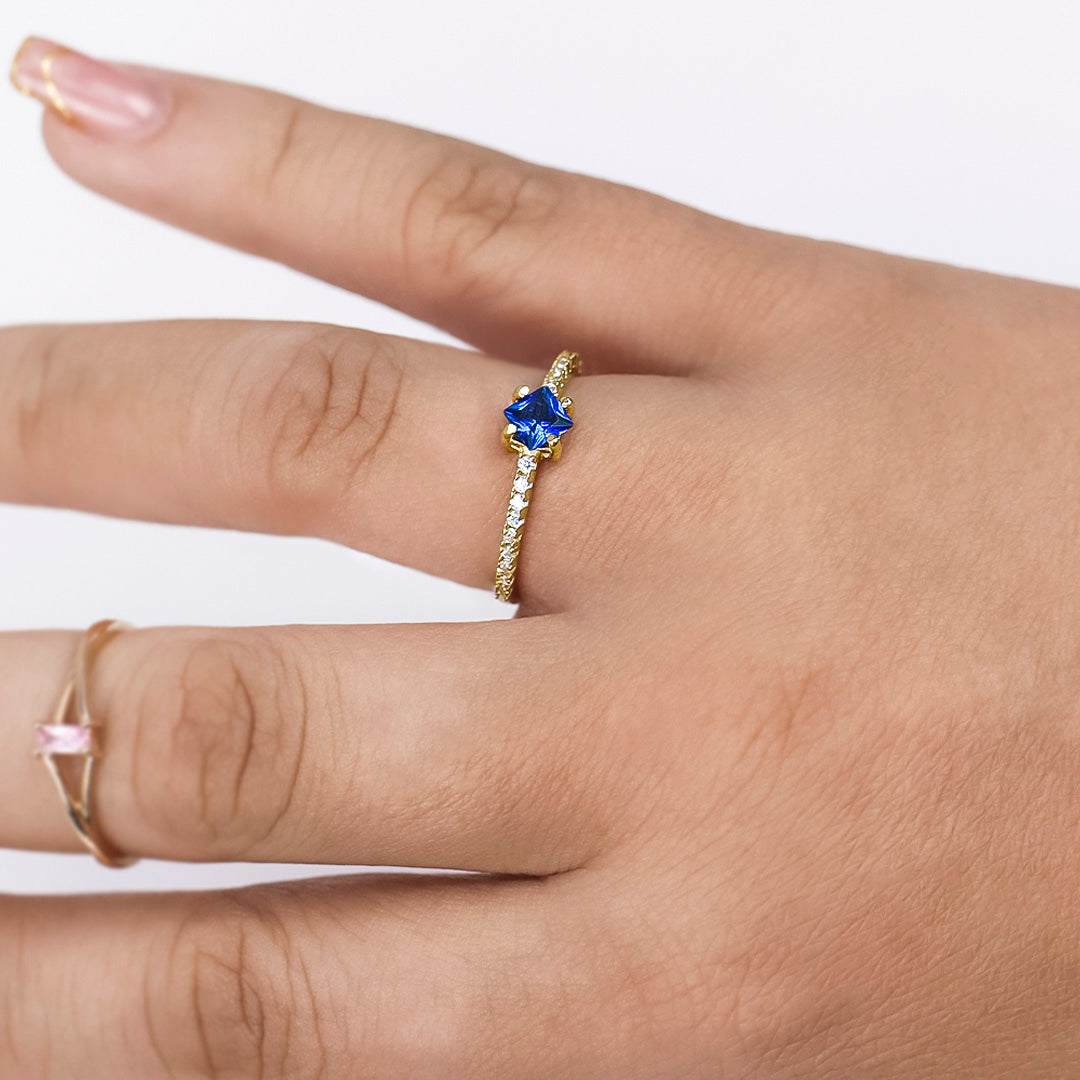 Mano de mujer con anillo en oro amarillo de 18 quilates con cristales de color blanco y cristal de color azul en forma de rombo en el centro, hecho en Joyería Caracas. 