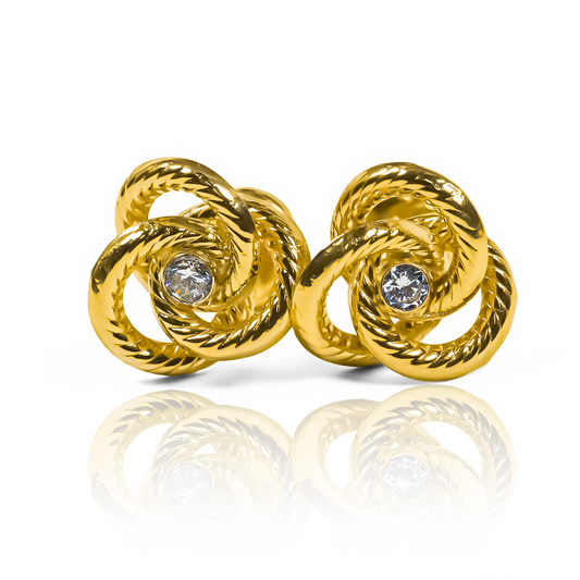 Disfruta de la elegancia y sofisticación con los Topitos Espiral lazo centro de cristal L. Hechos con oro 18K y diseñados por Joyería Caracas, estos pendientes son garantía para toda la vida. Añade un toque de lujo a tu look con estos hermosos pendientes.