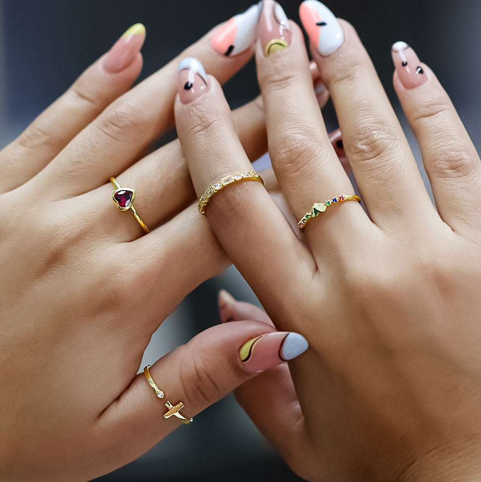 Mano de mujer usando anillo con corazón en el centro en oro amarillo de 18 quilates con cristales de distintos colores, hecho en Joyería Caracas. 