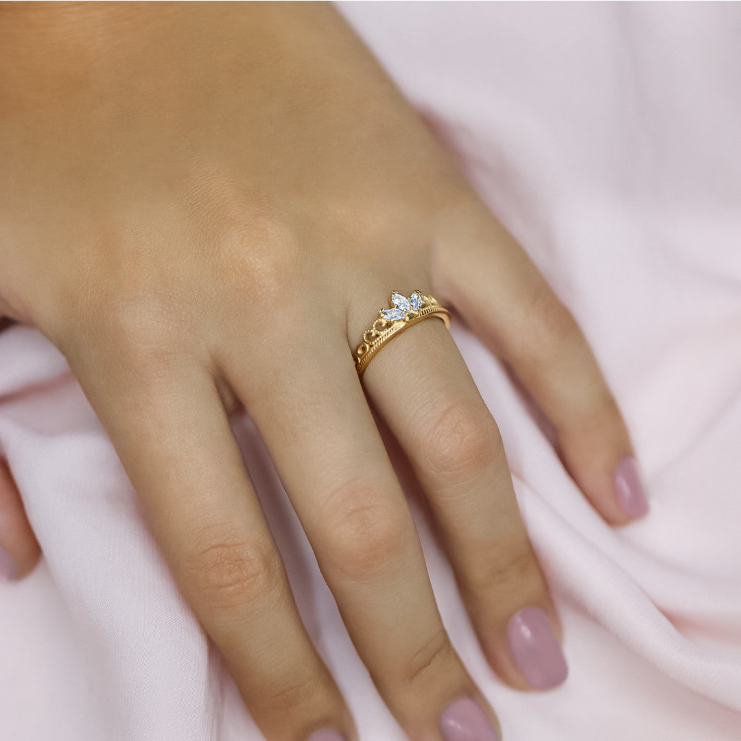 Mano de mujer con anillo en forma de corona en oro amarillo de 18 quilates con cristales en corte Marquise de color blanco, hecho en Joyería Caracas. 