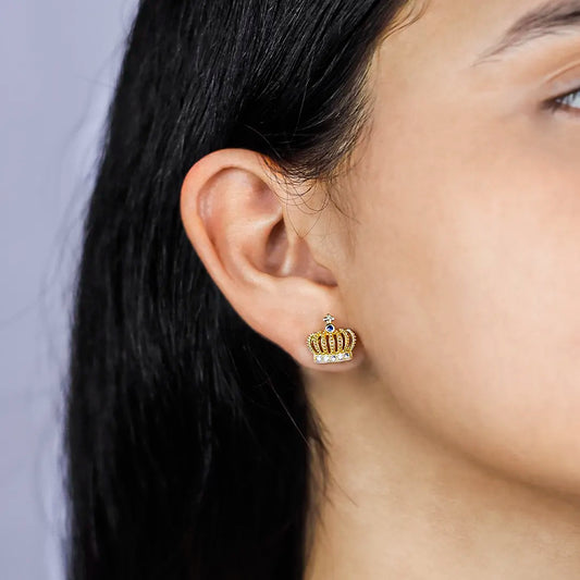 Oreja de mujer con topito en forma de corona en oro amarillo de 18 quilates con cristal de color azul en la punta y cristales de color blanco en la parte de abajo, hecho en Joyería Caracas. 