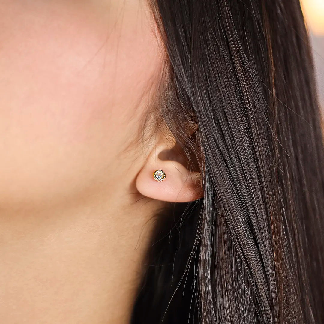 Oreja de mujer con topito en forma de dona entorchada en oro amarillo de 18 quilates con cristal de color blanco en el centro, hecho en Joyería Caracas. 