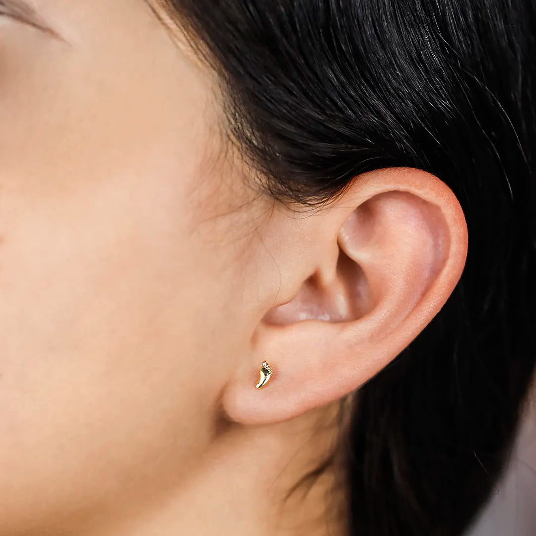 Oreja de mujer con topito en forma de pie en oro amarillo de 18 quilates.