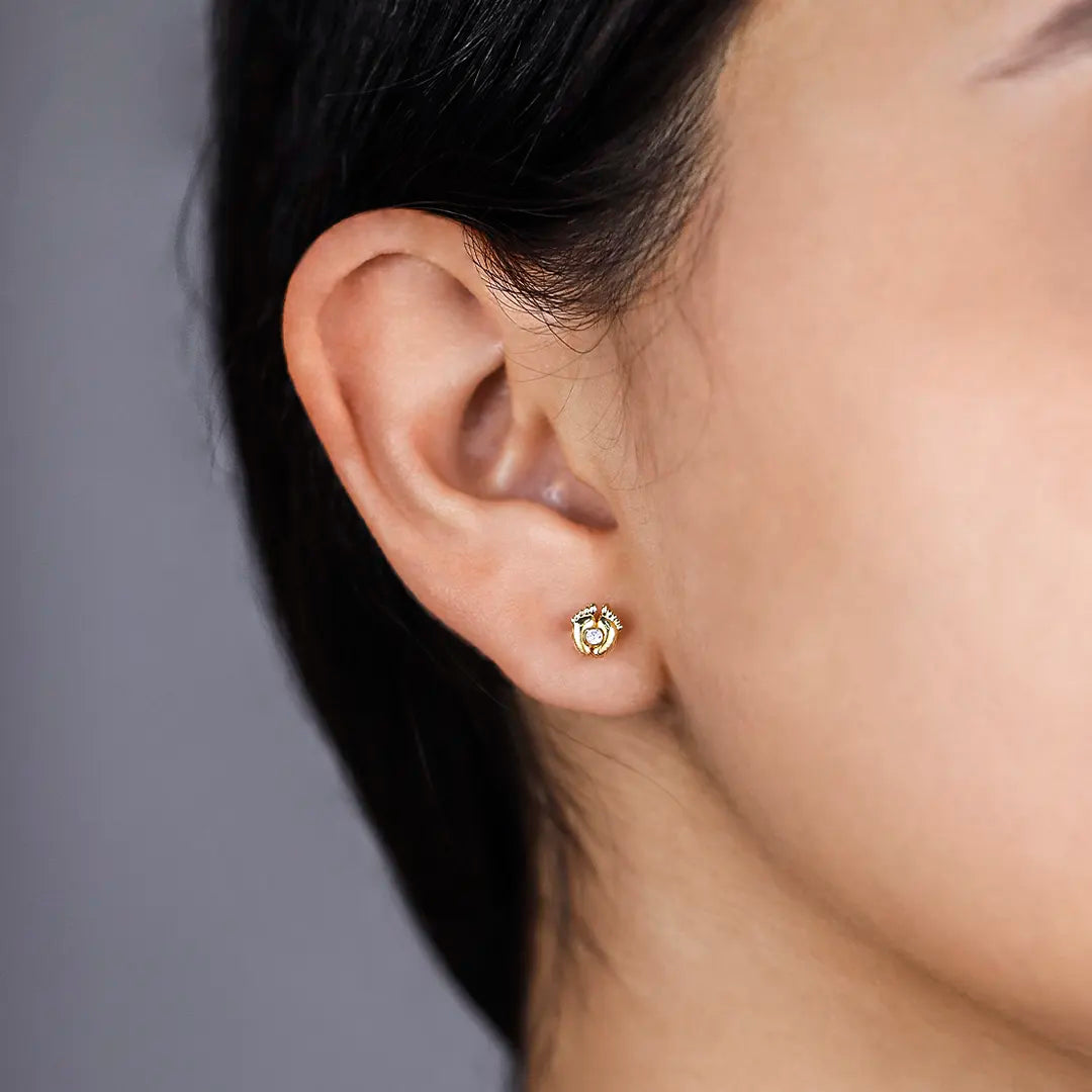 Oreja de mujer con topito en forma de dos pies unidos de oro amarillo de 18 quilates con un cristal en el centro de color blanco, hecho en joyeria caracas. 