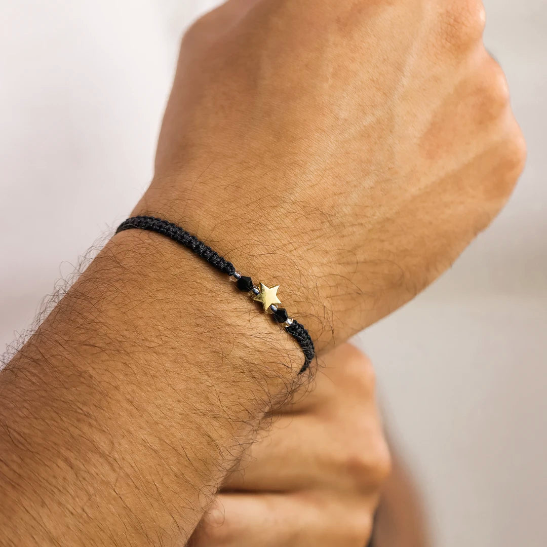 Mano de hombre con pulsera tejida en hilo negro, accesorios en color negro, blanco y dije de estrella en oro amarillo de 18 quilates de Joyería Caracas. 