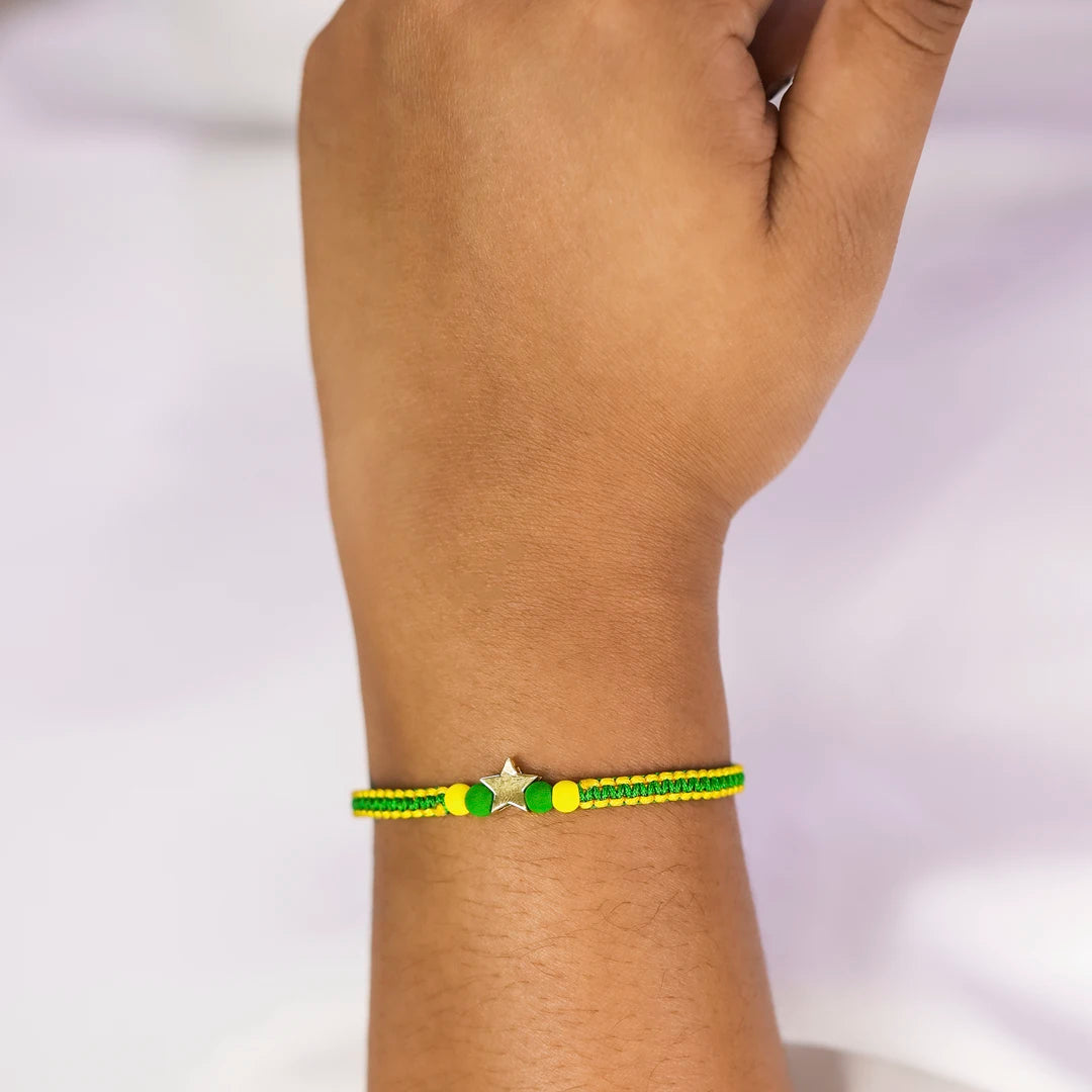 Mano de mujer con pulsera tejida en hilo verde, accesorios en color verde, amarillo y dije de estrella en oro amarillo de 18 quilates, hecho en Joyería Caracas. 